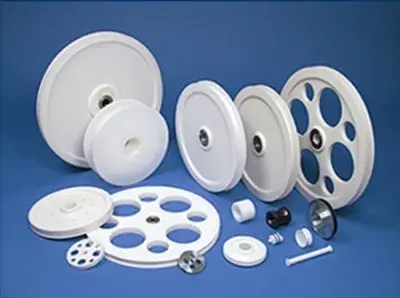 Assortment of white UHMW sheaves and pulleys in a range of diameters, several with weight-reduction holes, alongside smaller bushings and components